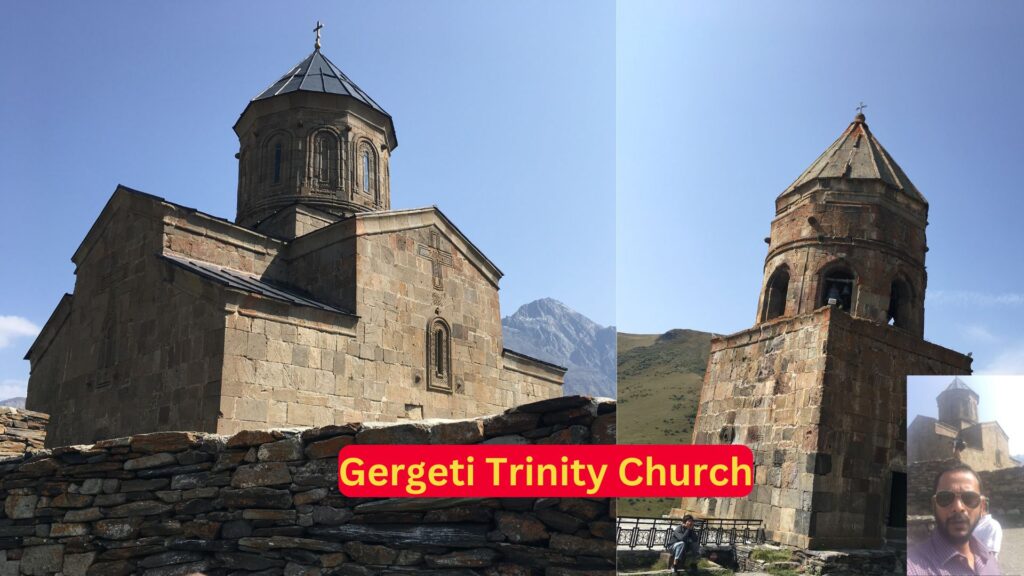 Man taking a picture in front of Gergeti Trinity Church with Mount Kazbek in the background.