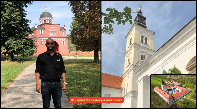 A man standing in front of Krušedol Monastery, surrounded by lush greenery and historic architecture.